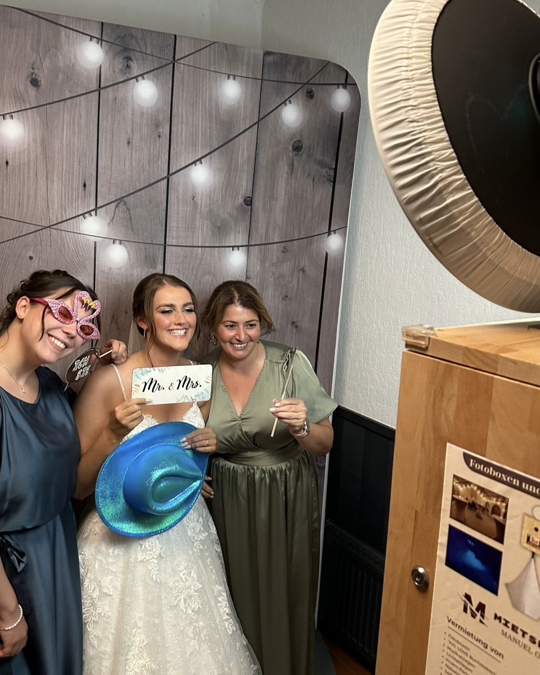 Bruid met twee gasten en props lacht voor de achtergrond met houtlook in de Overbeeke photobooth