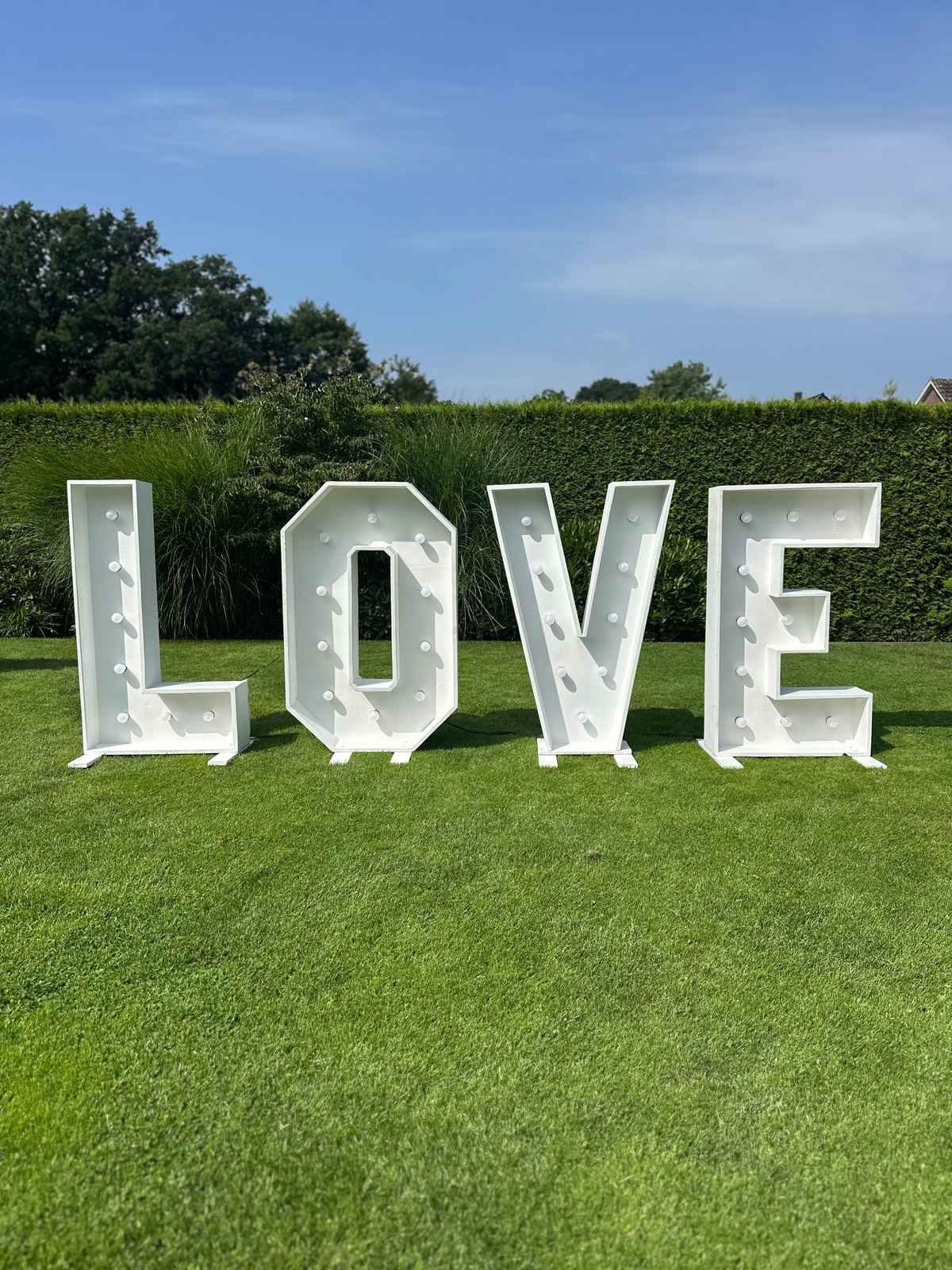 LOVE-Buchstaben tagsüber auf dem Rasen vor einer Hecke