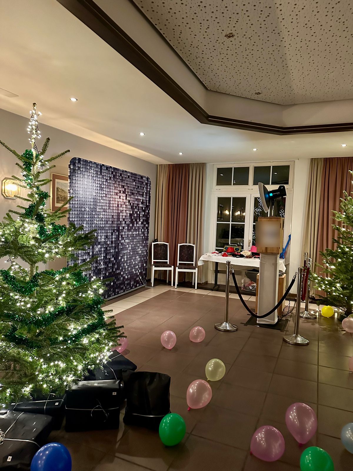 Photobooth met paillettenachtergrond en afzetpaaltjes op een kerstfeest tussen kerstbomen
